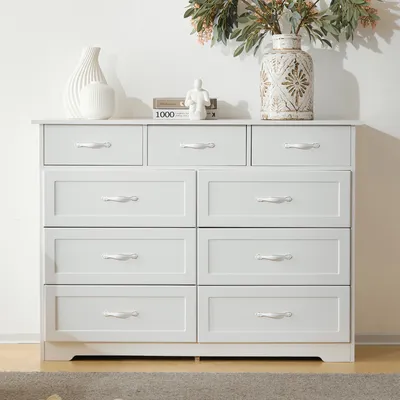 A white dresser with nine drawers is shown against a white background. Decorative items are placed on top of the dresser.