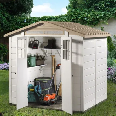 A white plastic garden shed with its doors open, filled with various gardening tools and equipment, set in a grassy backyard with green foliage in the background.