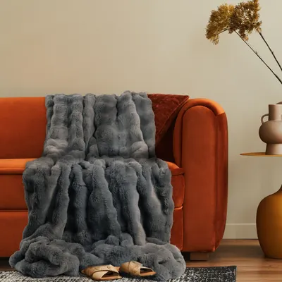 A plush gray blanket draped over an orange sofa, with slippers on the floor.