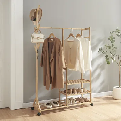A wooden garment rack with clothes and shoes on it, placed in a room with a gray wall and wooden floor.