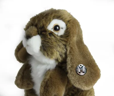 A close-up studio shot of a brown plush rabbit toy with floppy ears, set against a white background. A small circular emblem with a rabbit design is visible on its ear.