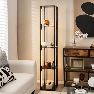 A modern living room scene featuring a tall, black shelf unit with integrated LED lighting, displaying decorative items. A white sofa is visible on the left, and a wooden console table with drawers is on the right.