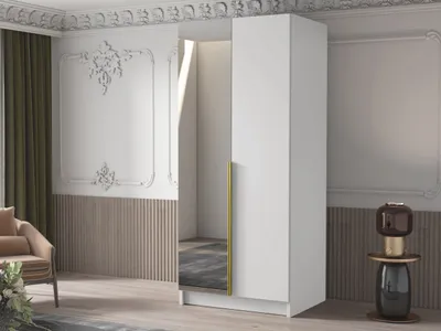 A modern white wardrobe with a gold handle and a mirrored door, placed in a well-decorated room with ornate wall moldings and a chair.