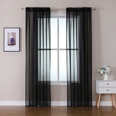 A window with black sheer curtains hanging in front of it, with a framed picture on the wall to the left and a nightstand with flowers to the right.