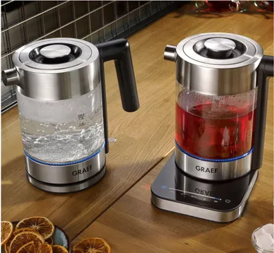 Two electric kettles on a wooden countertop, one filled with water and the other with red liquid.