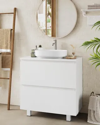 A white bathroom vanity with a vessel sink and faucet, set against a white brick wall.