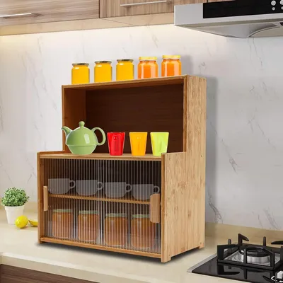 A kitchen counter with a bamboo storage cabinet organizer filled with jars, cups, and a teapot.