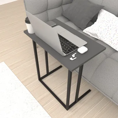 A laptop table is placed next to a sofa with a laptop, coffee cup, and earbuds on it.