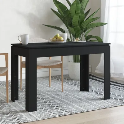 A black dining table is set in a room with a large plant and chairs.