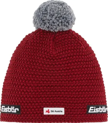 A red knitted beanie with a gray pom-pom on top, shown against a white background. It has two small black and white labels on the bottom edge.