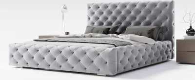 A tufted grey upholstered bed with pillows and a bedside table with a vase and a lamp.