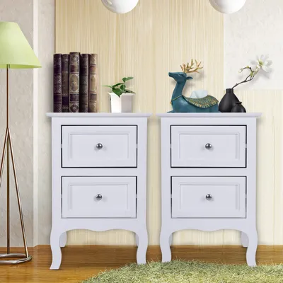 Two white bedside tables with drawers are shown in a room with a patterned wall and a floor lamp.