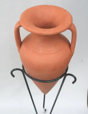 A terracotta amphora pot sits on a black metal stand against a white background.