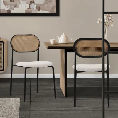 Two dining chairs with rattan backs and beige upholstered seats are placed around a wooden dining table in a room.