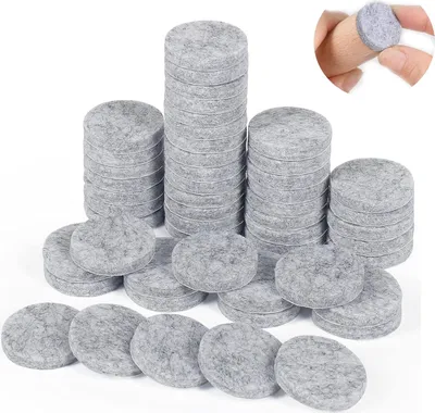 Stacks of round grey felt pads, also known as furniture sliders or felt gliders, are displayed on a white background. In the top right corner, a close-up shows a finger holding one of these felt pads against a wooden surface.
