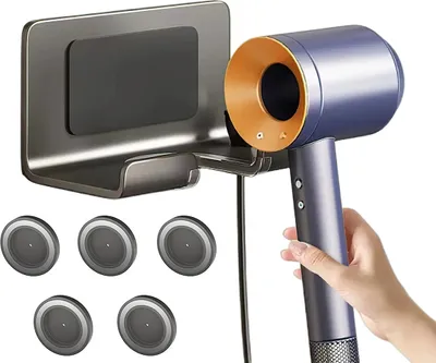 A hand holding a blue and gold hair dryer next to a gray wall-mounted holder.