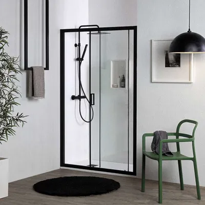 A modern bathroom with a black-framed shower enclosure, a green chair with a towel, and a black rug.