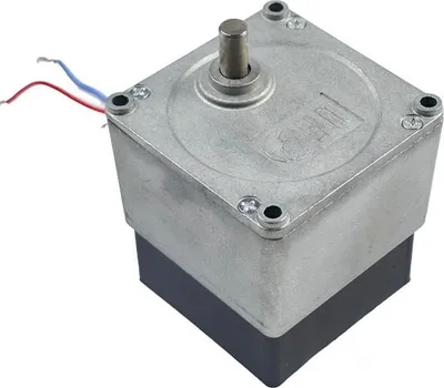 A close-up, angled view of a small, square motor with a metal casing and a black base, set against a white background. Two wires, one red and one blue, extend from the top left of the motor.