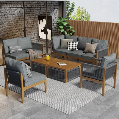 An outdoor living space with a sectional sofa, chairs, and coffee tables arranged on a rug.