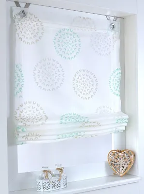 A white Roman blind with a circular pattern in turquoise and beige, hanging in a window frame.