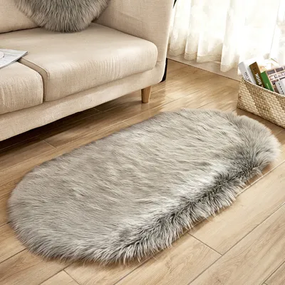 A fluffy gray rug is placed on a wooden floor next to a beige sofa. A basket of books is visible in the background.