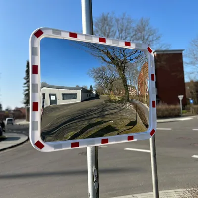 A convex traffic mirror with red and white markings on its frame, mounted on a pole at a street intersection.