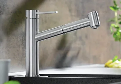 A modern kitchen faucet with a pull-out spray head is shown in a close-up shot, set against a textured backsplash and countertop.