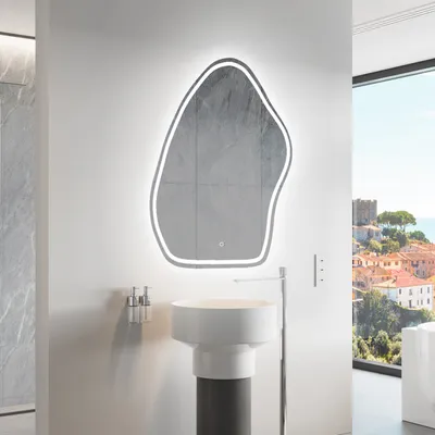 A modern bathroom with a unique, illuminated mirror above a pedestal sink, overlooking a scenic coastal town.