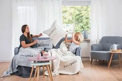 A woman and a child are relaxing on a sofa, surrounded by blankets and pillows.