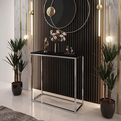 A modern console table with a black top and chrome frame, decorated with plants and a vase of flowers, set against a slatted wall and marble.