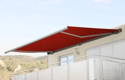A red retractable awning is extended from a building onto a balcony.