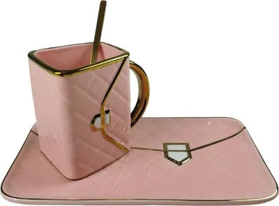 A pink ceramic cup and saucer set with a gold spoon, designed to resemble a handbag.