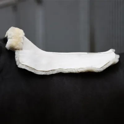 A close-up side view of a white saddle pad with sheepskin trim on a dark horse's back.