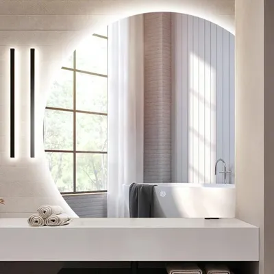 A modern bathroom with a large arched mirror reflecting a bathtub and window.
