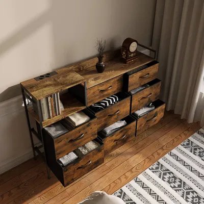 A dresser with multiple drawers and a shelf unit on the left, all in a vintage wood finish, placed on a wooden floor next to a rug.