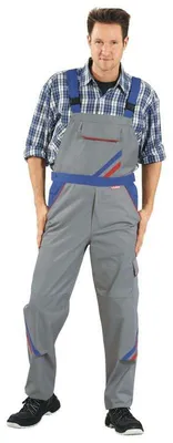 A man wearing work overalls and a plaid shirt, standing against a white background.
