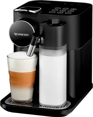 A black Nespresso coffee machine with a glass of latte and a milk carafe.