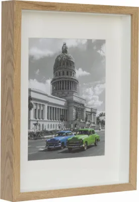 A framed picture of a building with two vintage cars in front.
