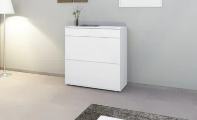 A white shoe cabinet is shown in a room with a floor lamp and a grey wall.