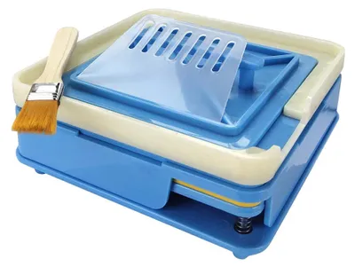 A blue and cream colored capsule filling machine with a brush on a white background.