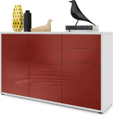 A white sideboard with bordeaux high-gloss doors and drawers, decorated with a yellow vase, a black vase, a wooden bird sculpture, and a black bird sculpture on top of books.