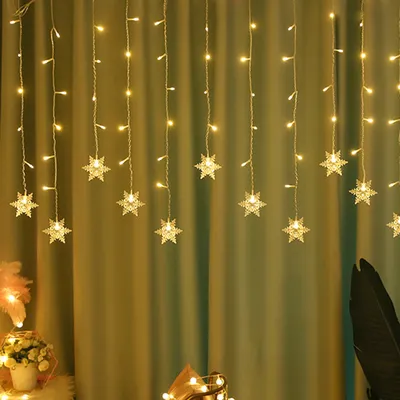 A string of snowflake-shaped LED lights hanging against a green curtain.