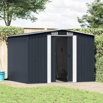 A dark gray metal garden shed with double doors is shown in an outdoor setting with a wooden deck and green grass.
