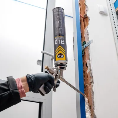 A person is using a can of spray foam to fill a gap in a wall next to a door frame.