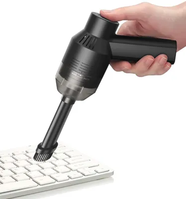 A hand holding a black mini vacuum cleaner and cleaning a white keyboard.