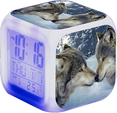 A cube-shaped digital alarm clock with wolf images on its sides and a digital display showing the time, day, month, date, and temperature. The clock is illuminated with blue light.