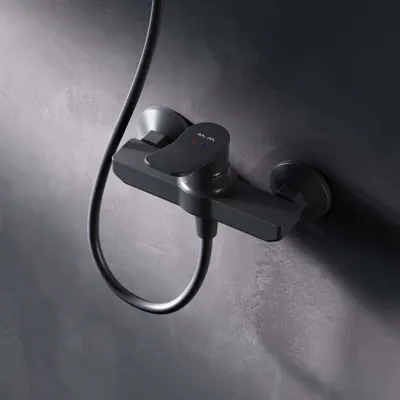 A black shower faucet mounted on a textured gray wall.