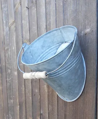 A galvanized metal bucket with a wooden handle is attached to a wooden fence.