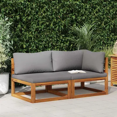 An outdoor sofa set with gray cushions is placed on a tiled patio in front of a lush green hedge.