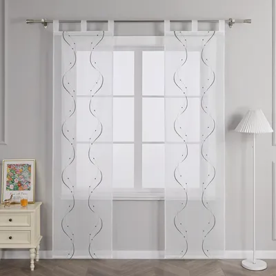 A window with sheer curtains and a bedside table with a framed picture and a lamp.